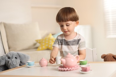 Photo of Cute little boy playing tea party with his toy elephant at table indoors