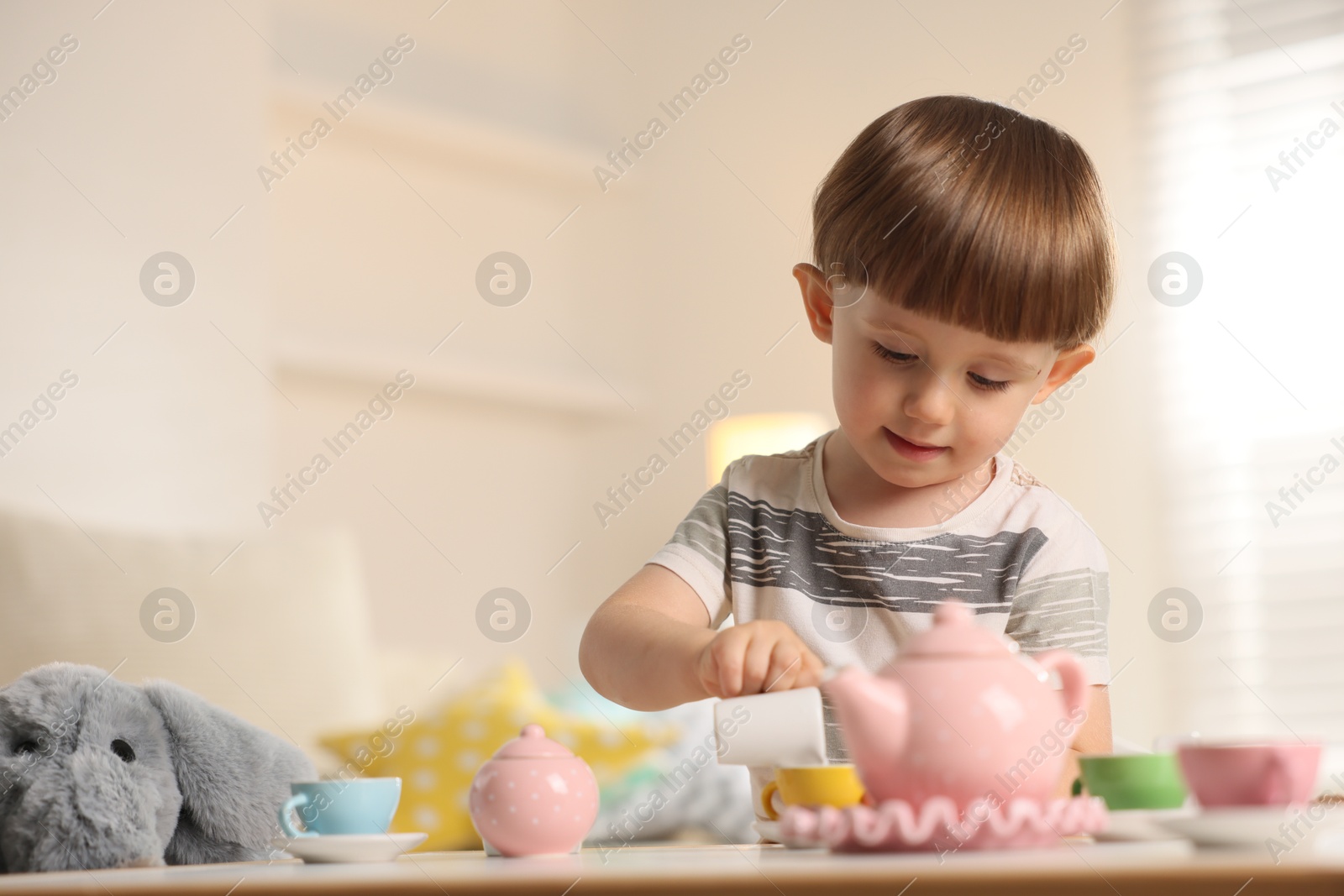 Photo of Cute little boy playing tea party with his toy elephant at table indoors. Space for text