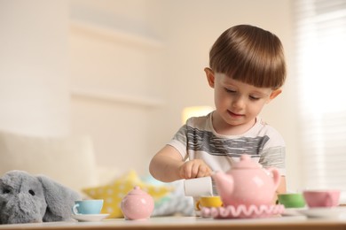 Photo of Cute little boy playing tea party with his toy elephant at table indoors. Space for text