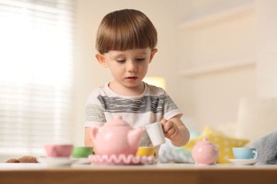 Photo of Cute little boy playing with toy tea set at table indoors