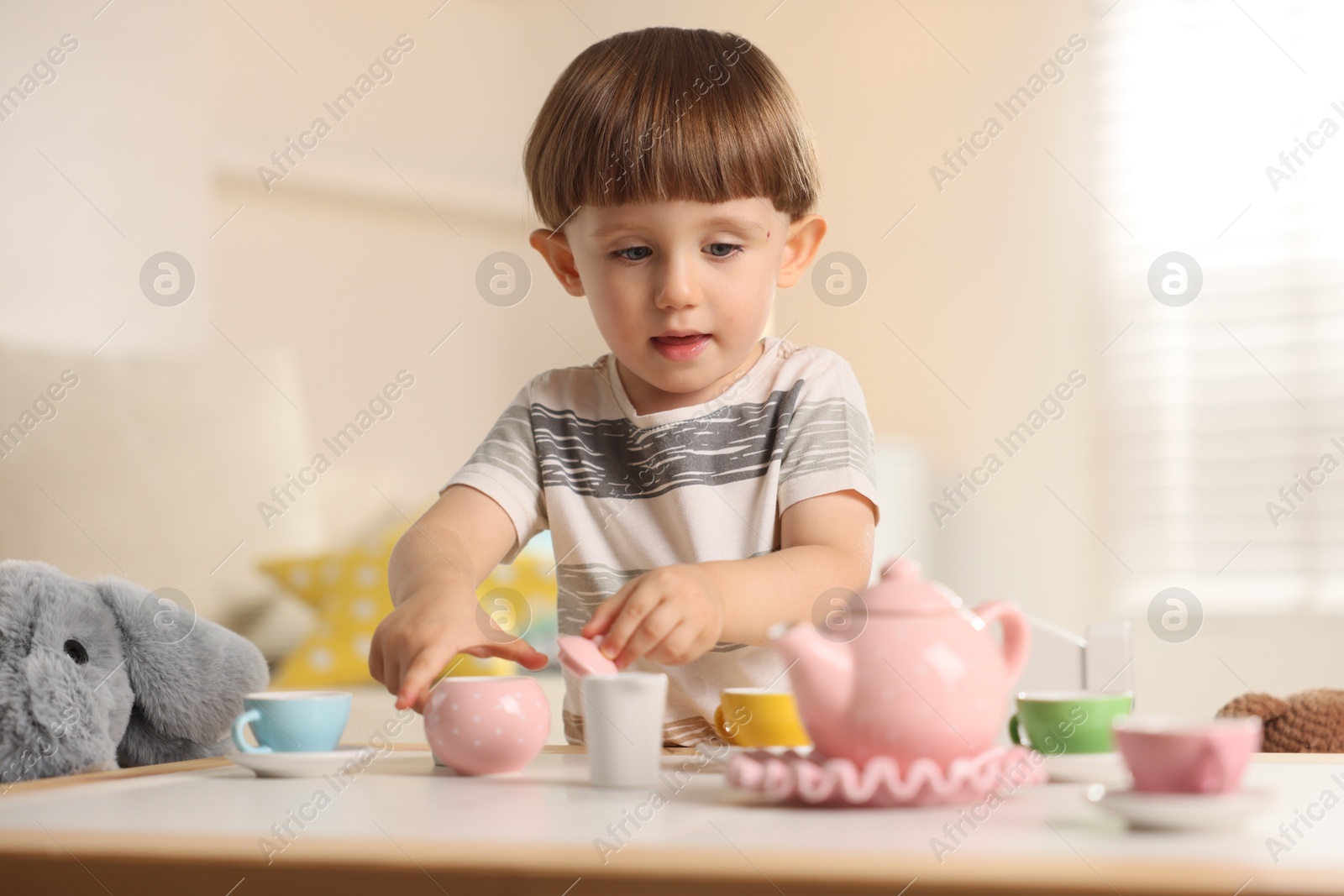 Photo of Cute little boy playing tea party with his toy elephant at table indoors