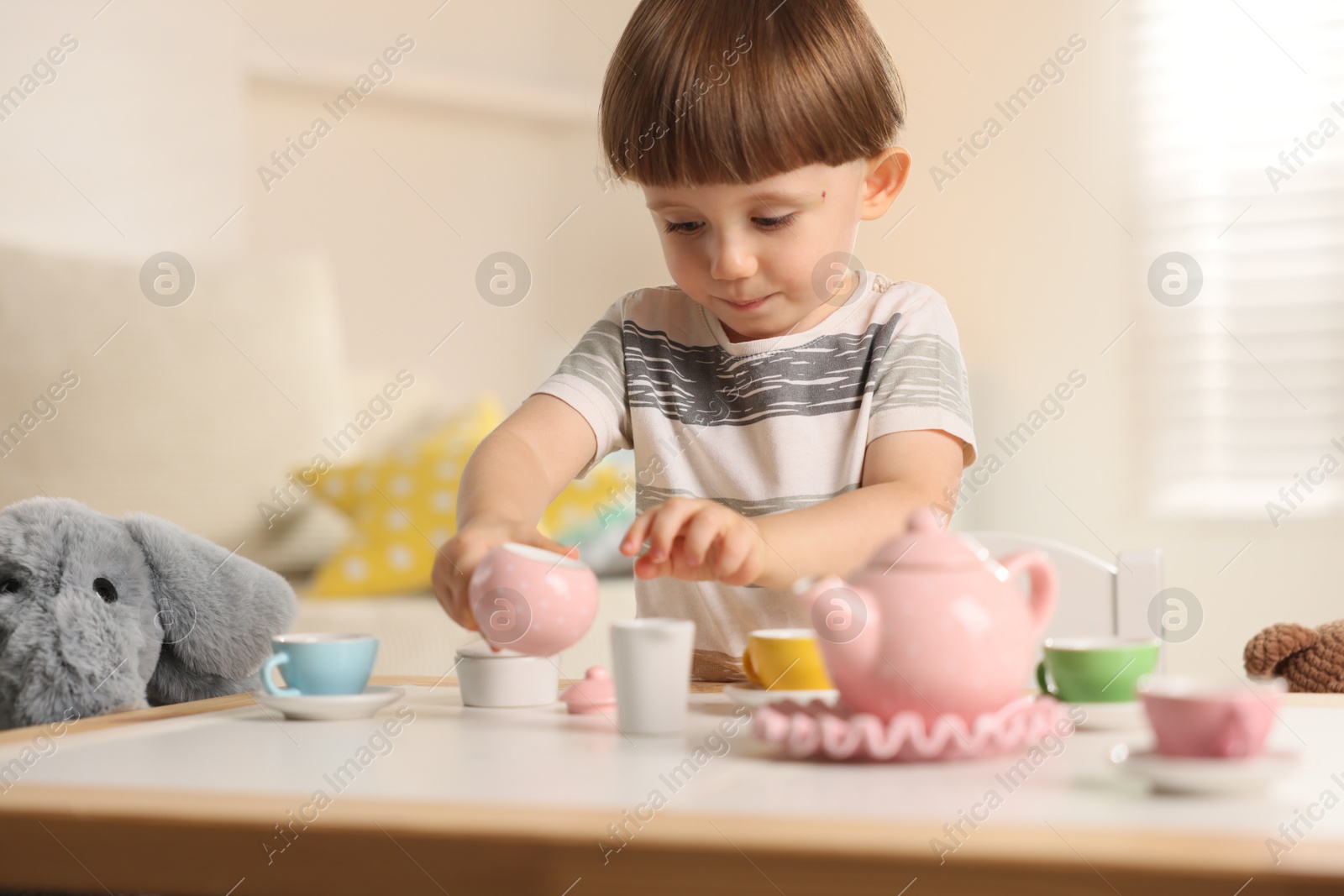 Photo of Cute little boy playing tea party with his toy elephant at table indoors