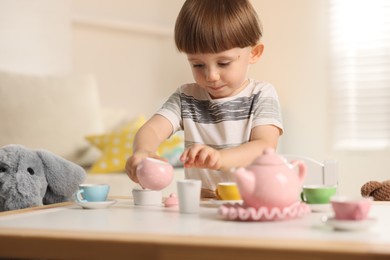 Photo of Cute little boy playing tea party with his toy elephant at table indoors