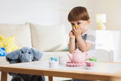 Photo of Cute little boy playing tea party with his toy elephant at table indoors. Space for text