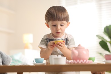 Photo of Cute little boy playing with toy tea set at table indoors