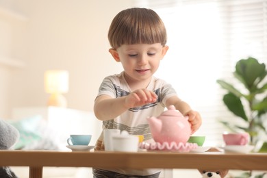 Photo of Cute little boy playing with toy tea set at table indoors