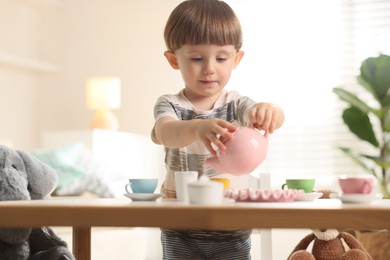 Photo of Cute little boy playing tea party with his toys at table indoors