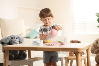 Photo of Cute little boy playing tea party with his toys at table indoors