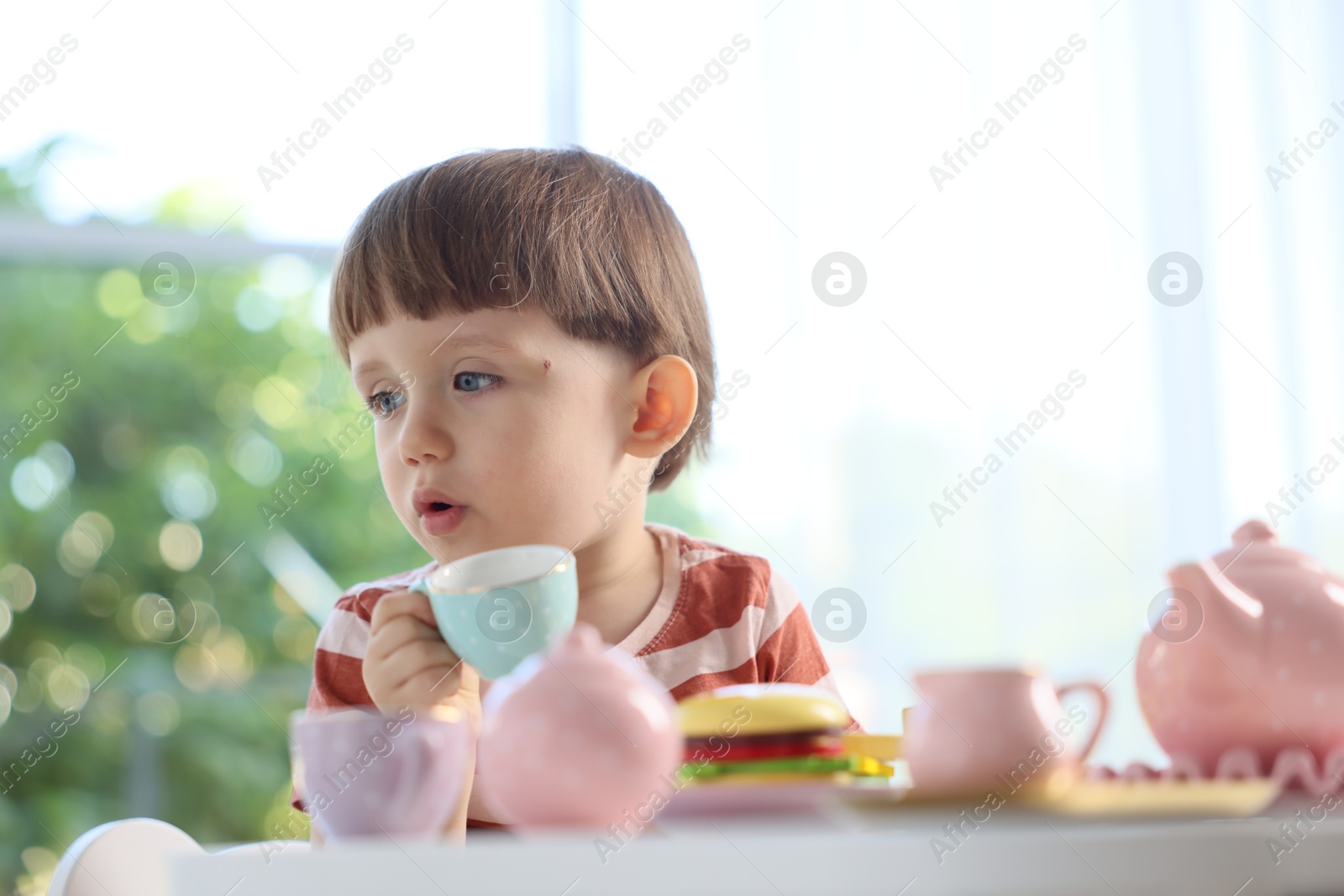 Photo of Cute little boy playing with toy tea set at table indoors