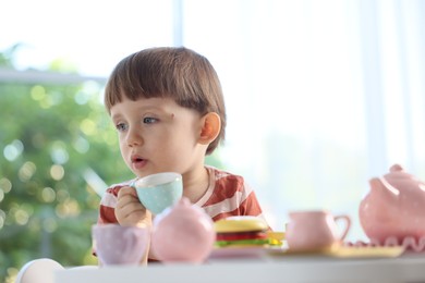 Photo of Cute little boy playing with toy tea set at table indoors