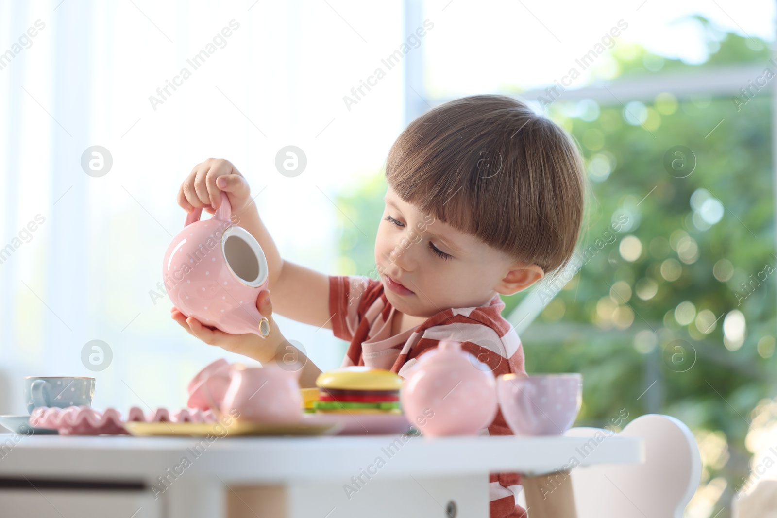 Photo of Cute little boy playing with toy tea set at table indoors