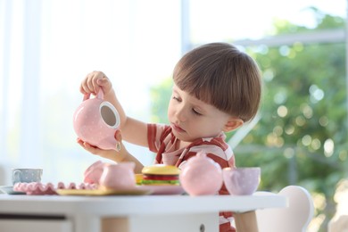 Photo of Cute little boy playing with toy tea set at table indoors