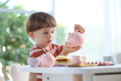 Photo of Cute little boy playing with toy tea set at table indoors