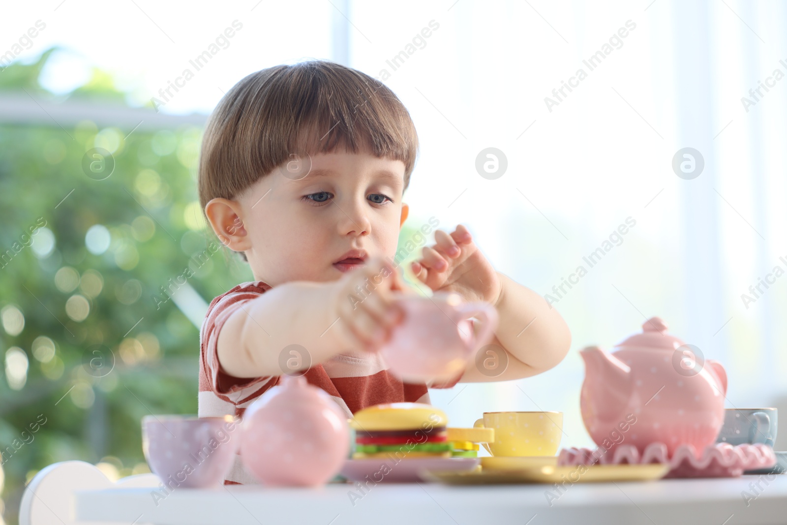 Photo of Cute little boy playing with toy tea set at table indoors