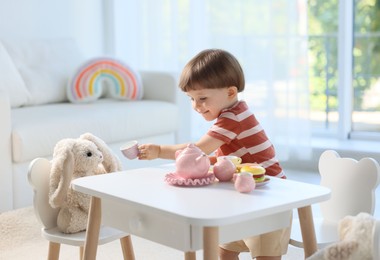 Photo of Cute little boy playing tea party with his toy bunny at table indoors