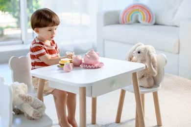 Photo of Cute little boy playing tea party with his toys at table indoors