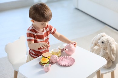Photo of Cute little boy playing tea party with his toy bunny at table indoors. Space for text