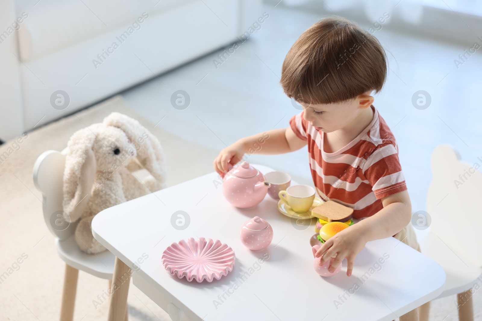 Photo of Cute little boy playing tea party with his toy bunny at table indoors