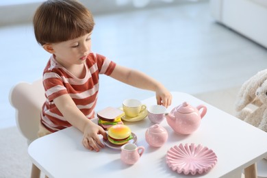 Photo of Cute little boy playing tea party with his toy bunny at table indoors. Space for text
