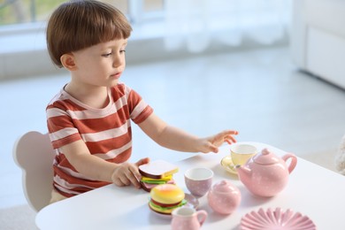 Photo of Cute little boy playing with toy tea set at table indoors. Space for text
