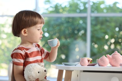Photo of Cute little boy playing tea party with his toy sheep at table indoors. Space for text