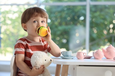 Photo of Cute little boy playing tea party with his toy sheep at table indoors. Space for text