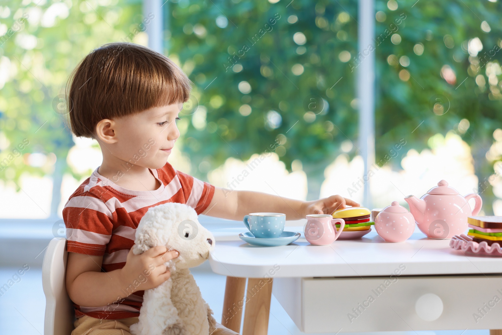 Photo of Cute little boy playing tea party with his toy sheep at table indoors. Space for text