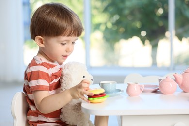 Photo of Cute little boy playing tea party with his toy sheep at table indoors. Space for text