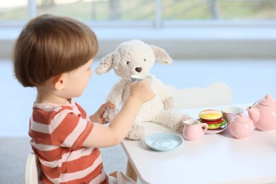 Photo of Cute little boy playing tea party with his toy sheep at table indoors