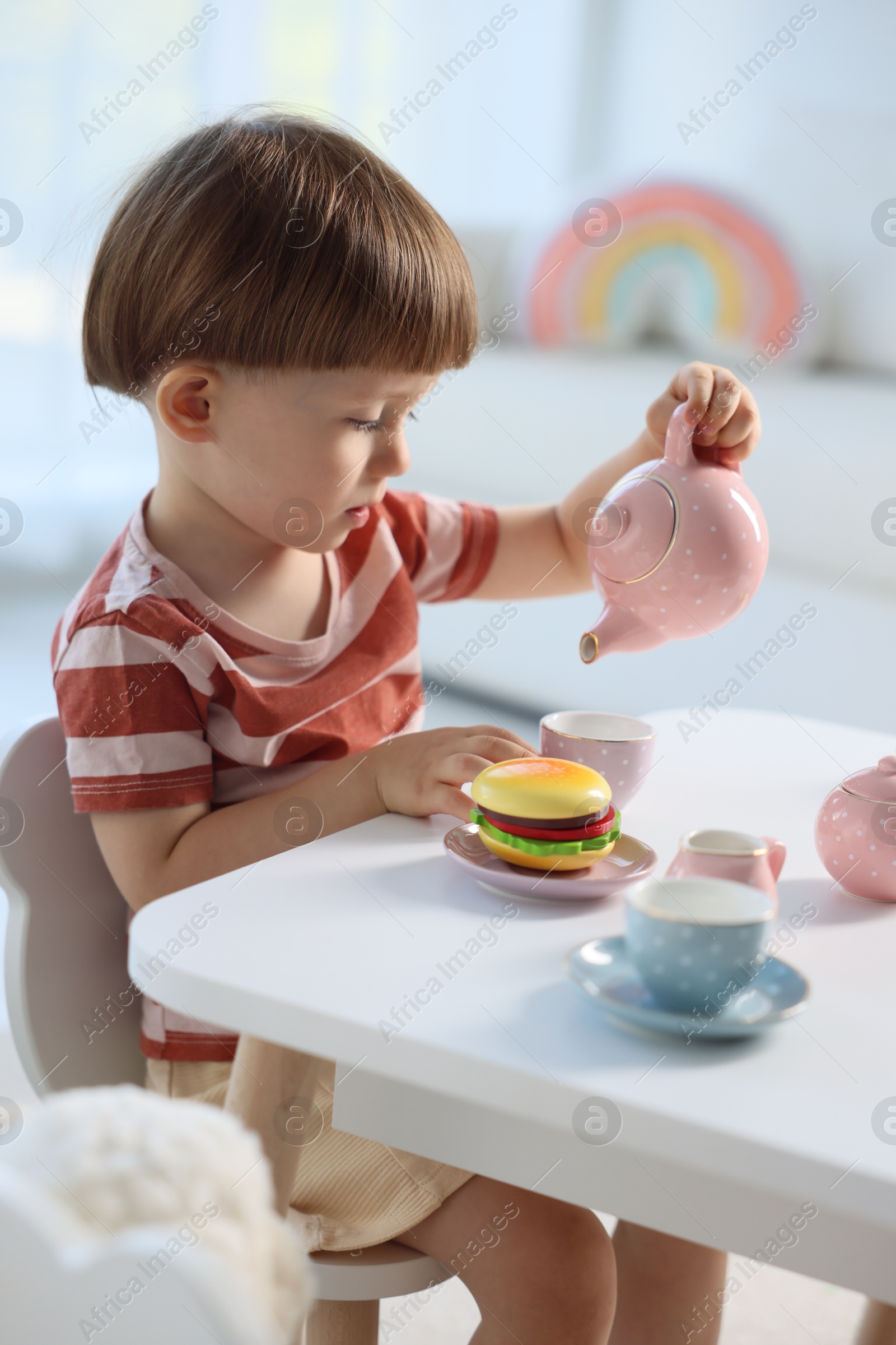 Photo of Cute little boy playing with toy tea set at table indoors