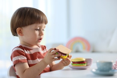 Photo of Cute little boy playing with toy tea set at table indoors. Space for text