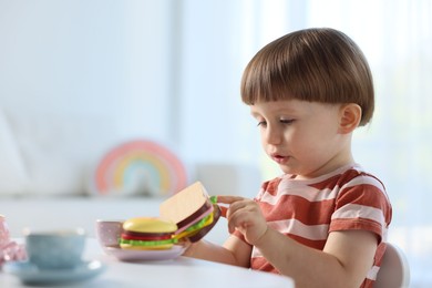 Photo of Cute little boy playing with toy tea set at table indoors. Space for text