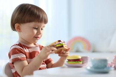 Photo of Cute little boy playing with toy tea set at table indoors. Space for text