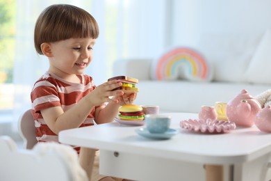 Photo of Cute little boy playing with toy tea set at table indoors. Space for text
