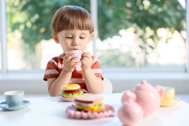 Photo of Cute little boy playing with toy tea set at table indoors. Space for text