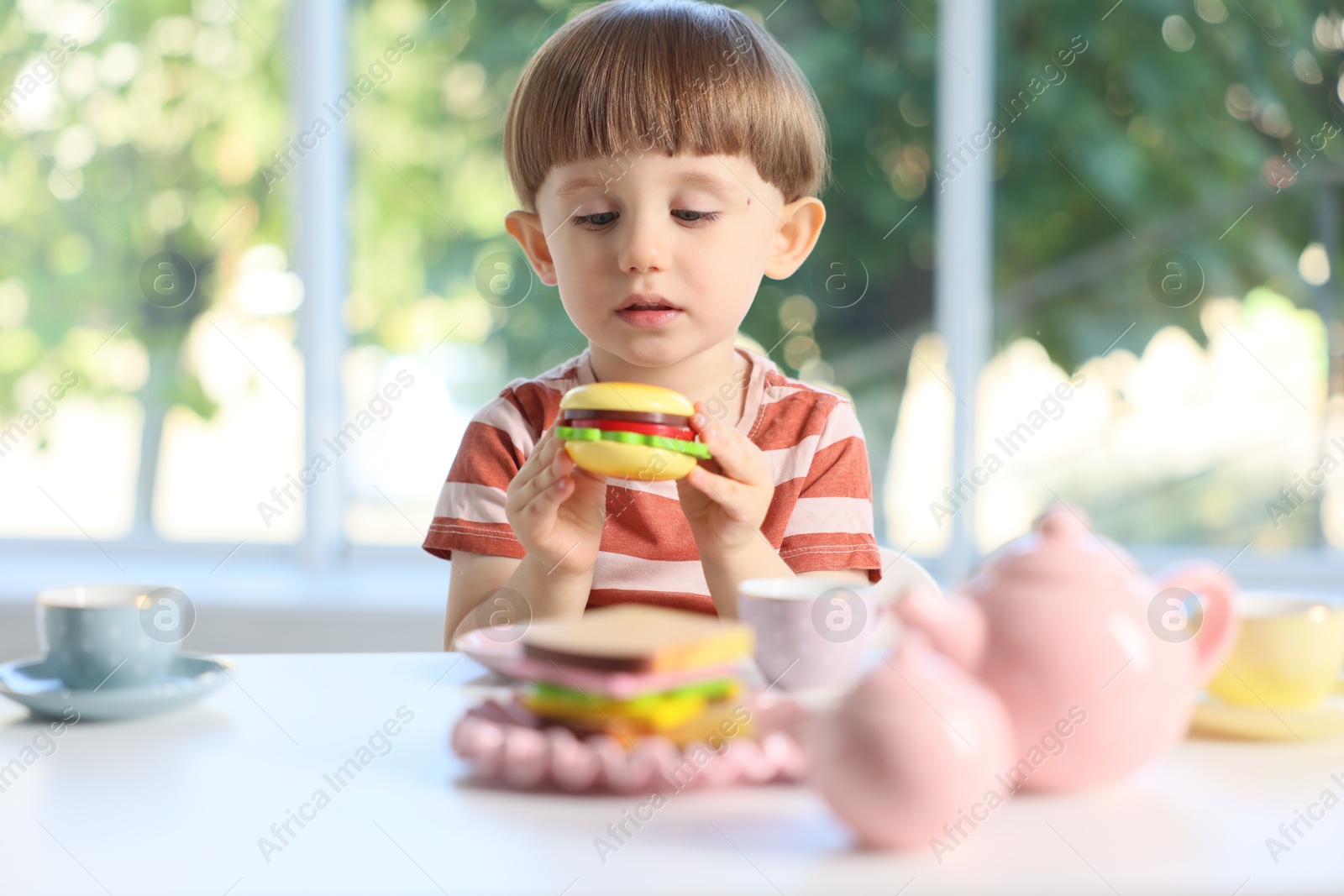Photo of Cute little boy playing with toy tea set at table indoors