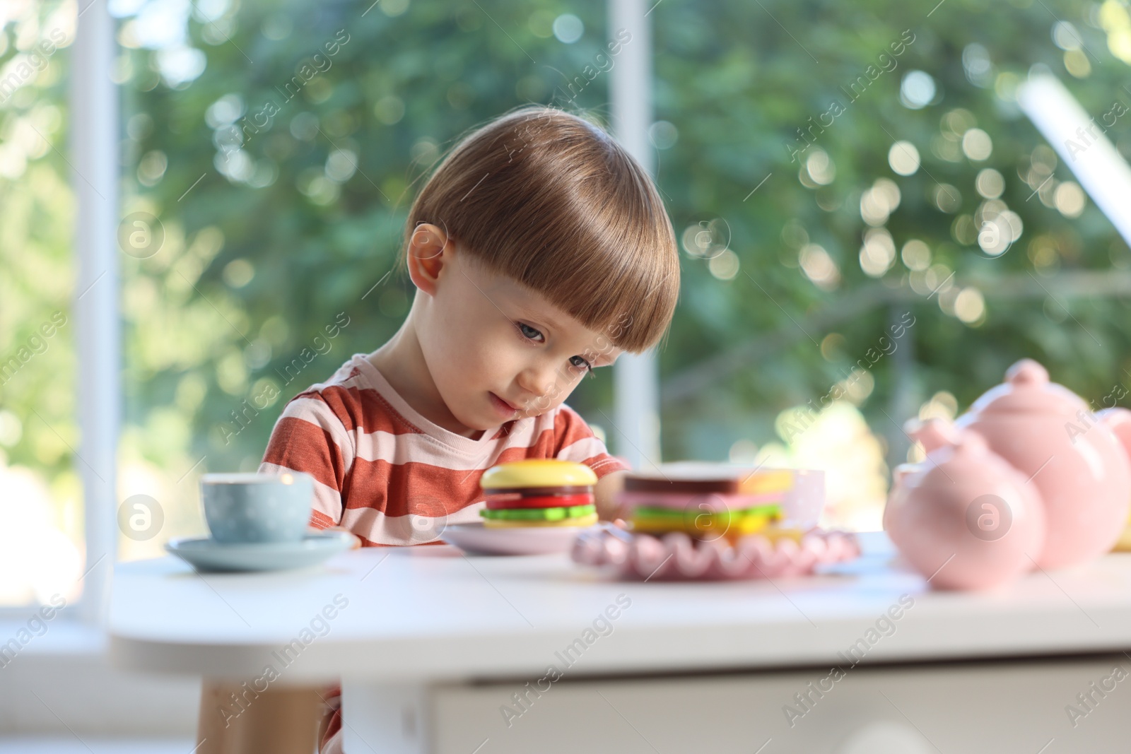 Photo of Cute little boy playing with toy tea set at table indoors
