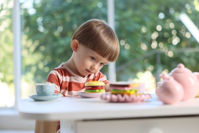 Photo of Cute little boy playing with toy tea set at table indoors