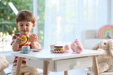 Photo of Cute little boy playing tea party with his toy bunny at table indoors. Space for text
