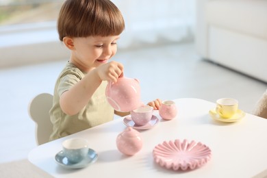 Photo of Cute little boy playing with toy tea set at table indoors. Space for text