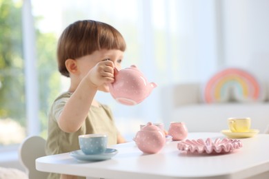 Photo of Cute little boy playing with toy tea set at table indoors. Space for text