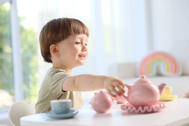 Photo of Cute little boy playing with toy tea set at table indoors. Space for text