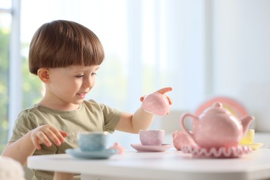Photo of Cute little boy playing with toy tea set at table indoors. Space for text