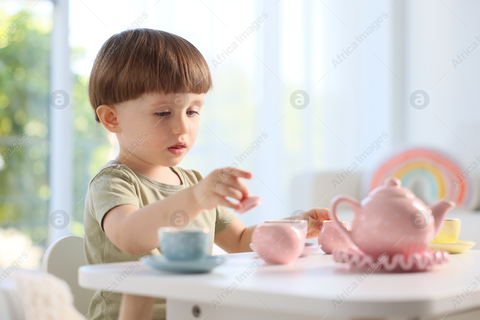Photo of Cute little boy playing with toy tea set at table indoors. Space for text