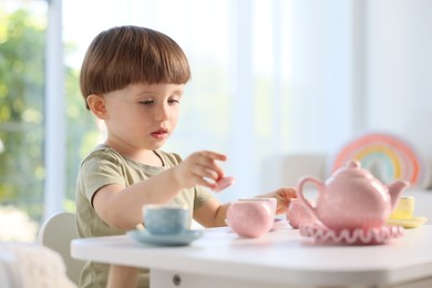 Photo of Cute little boy playing with toy tea set at table indoors. Space for text