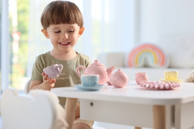 Photo of Cute little boy playing with toy tea set at table indoors. Space for text