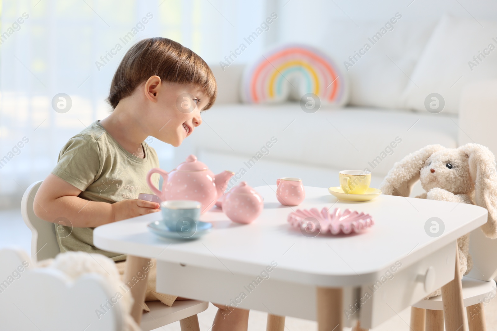 Photo of Cute little boy playing tea party with his toys at table indoors. Space for text