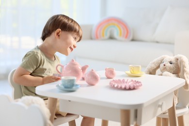 Photo of Cute little boy playing tea party with his toys at table indoors. Space for text