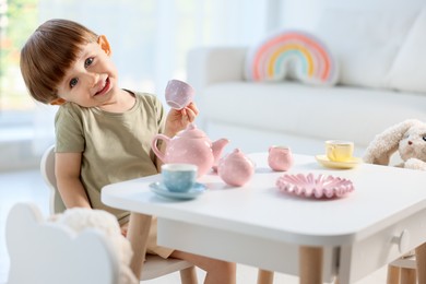 Photo of Cute little boy playing tea party with his toys at table indoors. Space for text