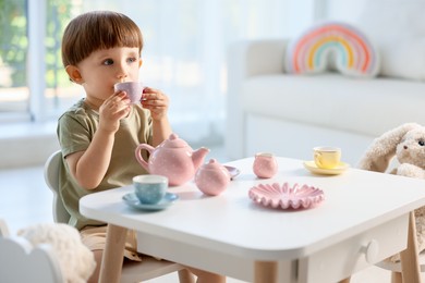 Photo of Cute little boy playing tea party with his toys at table indoors. Space for text